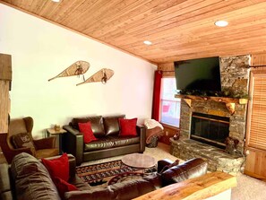 Ein gemütliches Wohnzimmer mit Kamin aus Stein, Ledersofas und einem Fernseher.