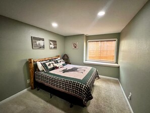Ein Schlafzimmer mit einem Bett, einem Fenster mit Jalousien und zwei Wandbildern.