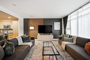 A modern living room with a sofa set, a coffee table, a flat-screen TV, and a kitchen area in the background. - The City Cottage, Sleeps 16 near the CN Tower with a 85 inch TV! (Toronto)