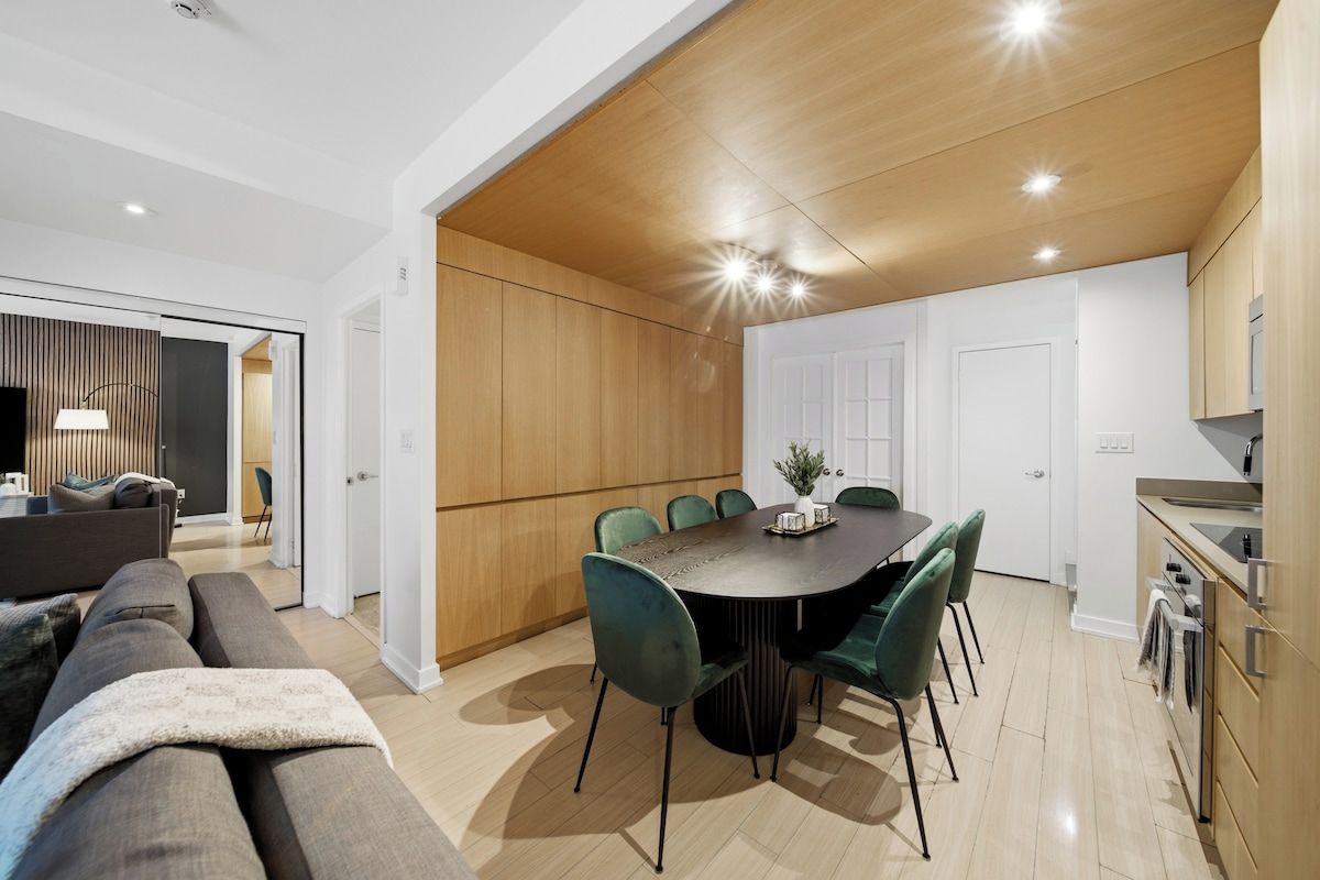 A modern living room with a sofa, a dining table with chairs, and a kitchen area with wooden cabinets.