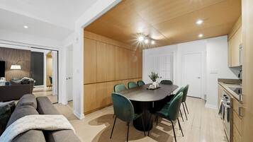 A modern living room with a sofa, a dining table with chairs, and a kitchen area with wooden cabinets.