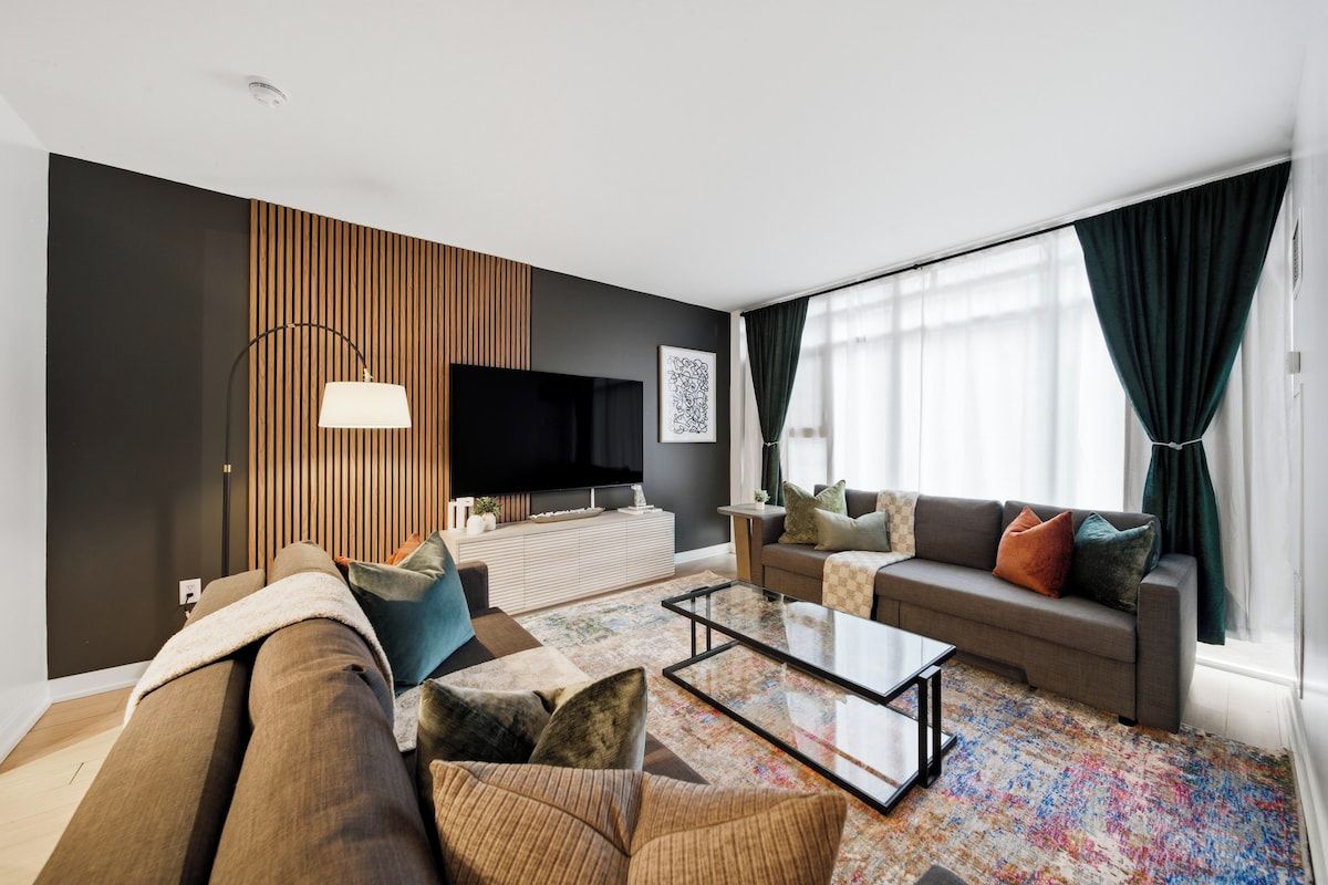 Un salon moderne avec un canapé, une table basse, un téléviseur et un tapis à motifs.