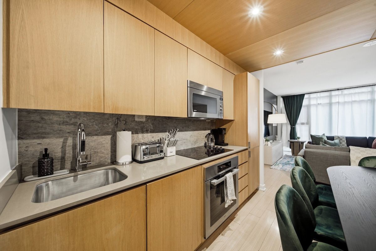 A modern kitchen with a built-in microwave, a sink, and a stove. There is a dining area with a table and chairs.