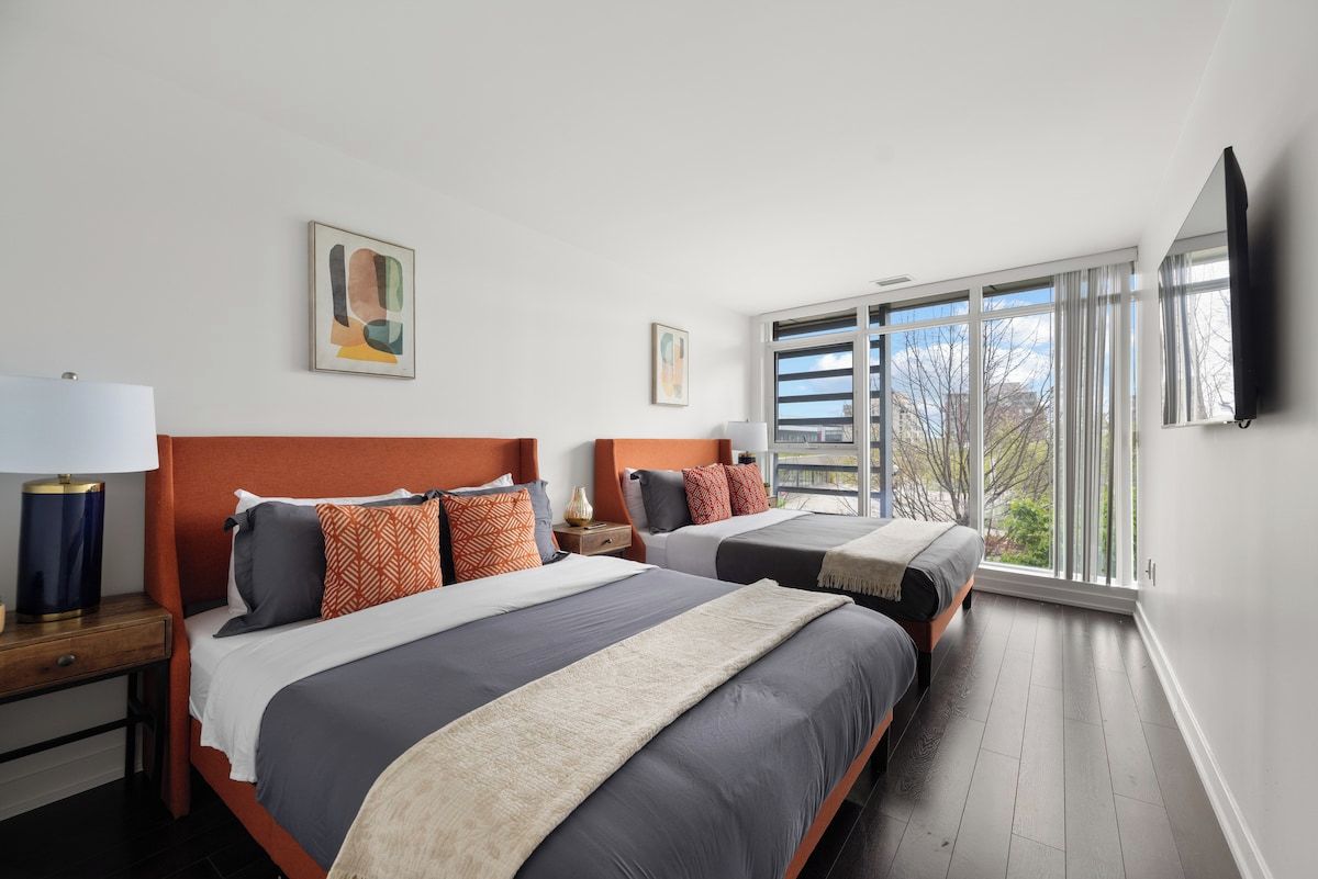 Une chambre d’hôtel avec deux lits, une grande fenêtre et un téléviseur à écran plat.