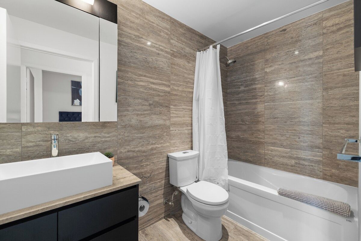 Une salle de bain moderne avec un grand miroir, un lavabo blanc, des toilettes et une baignoire.