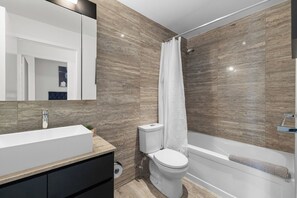 A modern bathroom with a large mirror, a white sink, a toilet, and a bathtub. - Luxury 4BR Home, King Bed, Sleeps 12 with Parking! (Toronto)