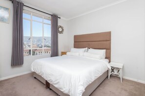 A bedroom with a large bed, a nightstand, a window with curtains, and a view of a cityscape. - Gorgeous 2-bedroom apartment in Cape Town near vibrant city life (Cape Town)