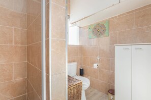 A bathroom with beige tiles, a toilet, a bidet, a white cabinet, and a decorative wall piece. - Gorgeous 2-bedroom apartment in Cape Town near vibrant city life (Cape Town)