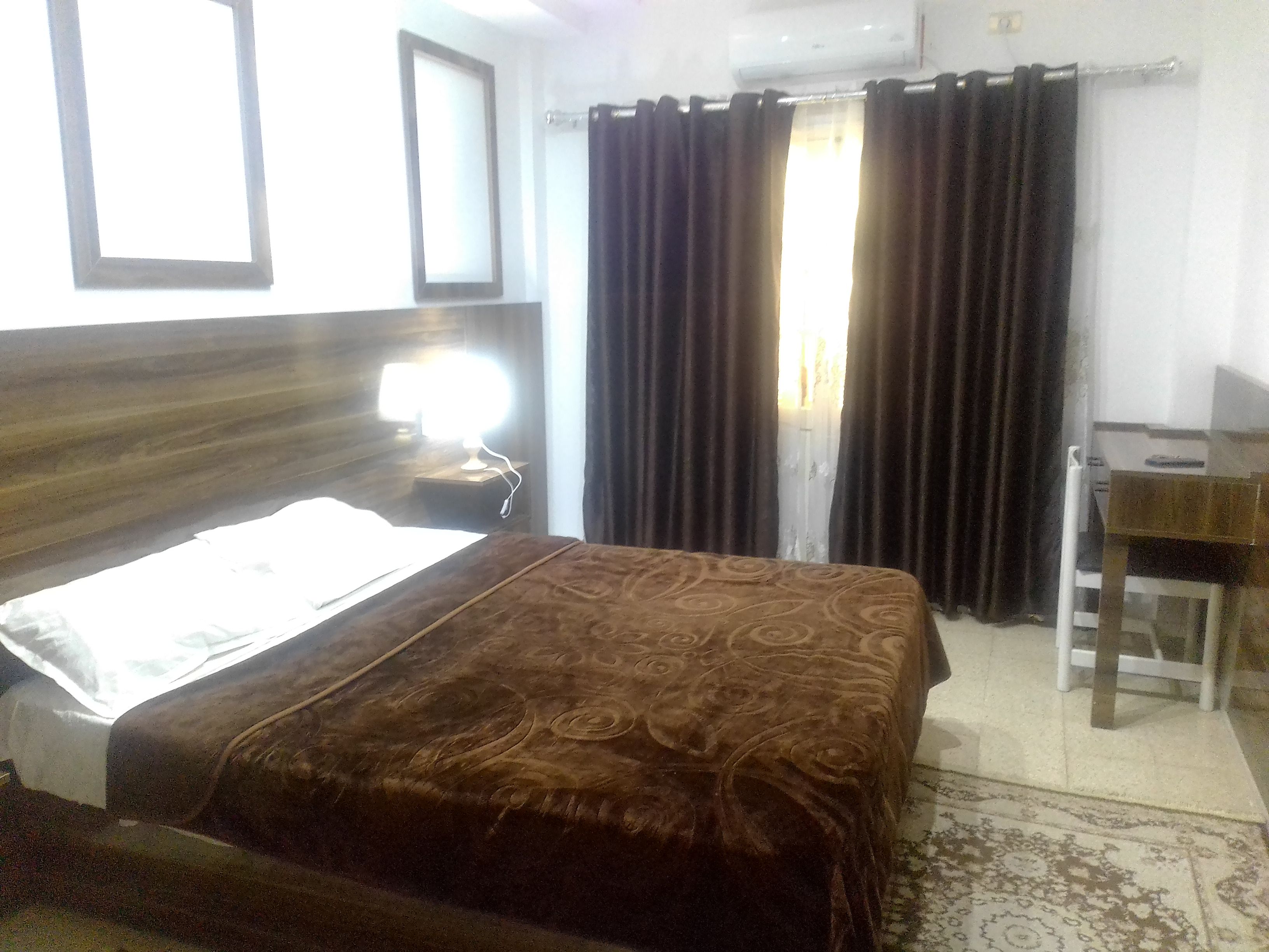 A hotel room with a bed, a desk, and a window with curtains.