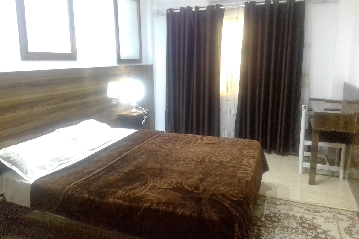 A hotel room with a bed, a desk, and a window with curtains.