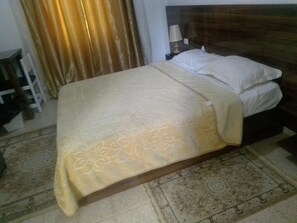 A bed with a patterned bedspread, a wooden headboard, and a nightstand with a lamp. - hotel amilcar (Tataouine)