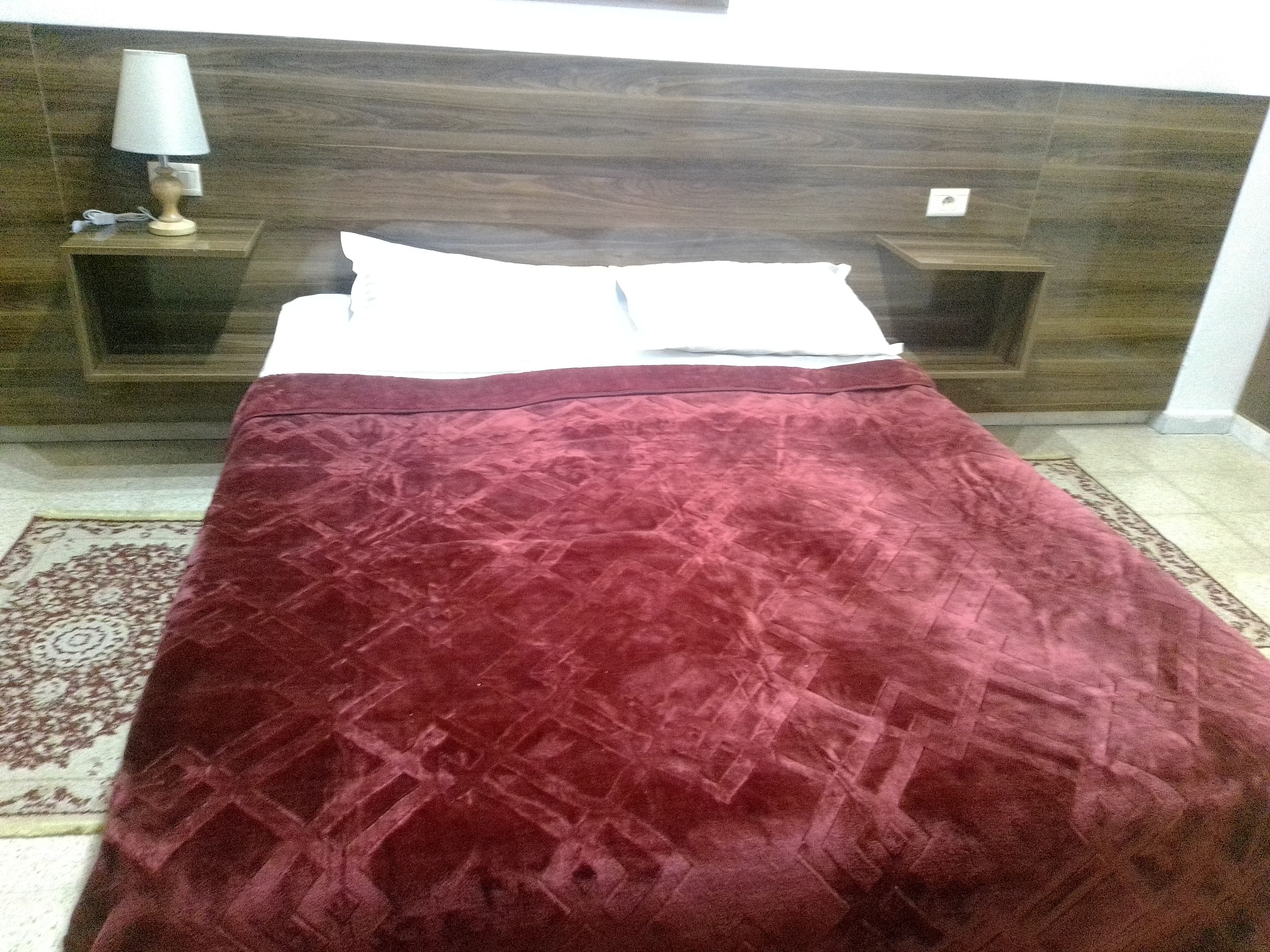 A bed with a patterned bedspread, a bedside table with a lamp, and a nightstand with a power outlet.