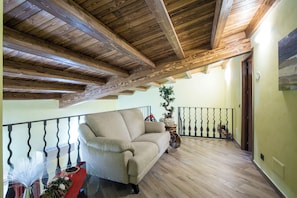 A cozy room with a wooden ceiling, a cushioned sofa, a dining table with a glass top, and a potted plant. - New Listing (Malvagna)