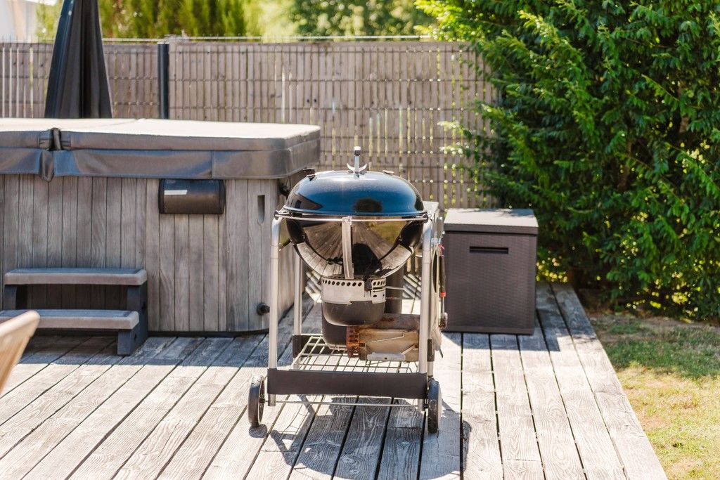A portable grill on a wooden deck with a hot tub and steps in the background.