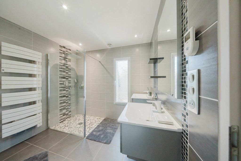 A modern bathroom with a glass shower enclosure, a white vanity, and a large mirror.