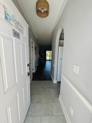 Un couloir avec une porte portant l’inscription « 204 », un luminaire suspendu en osier au plafond et une vue sur une pièce dont le sol est recouvert d’une moquette bleue.