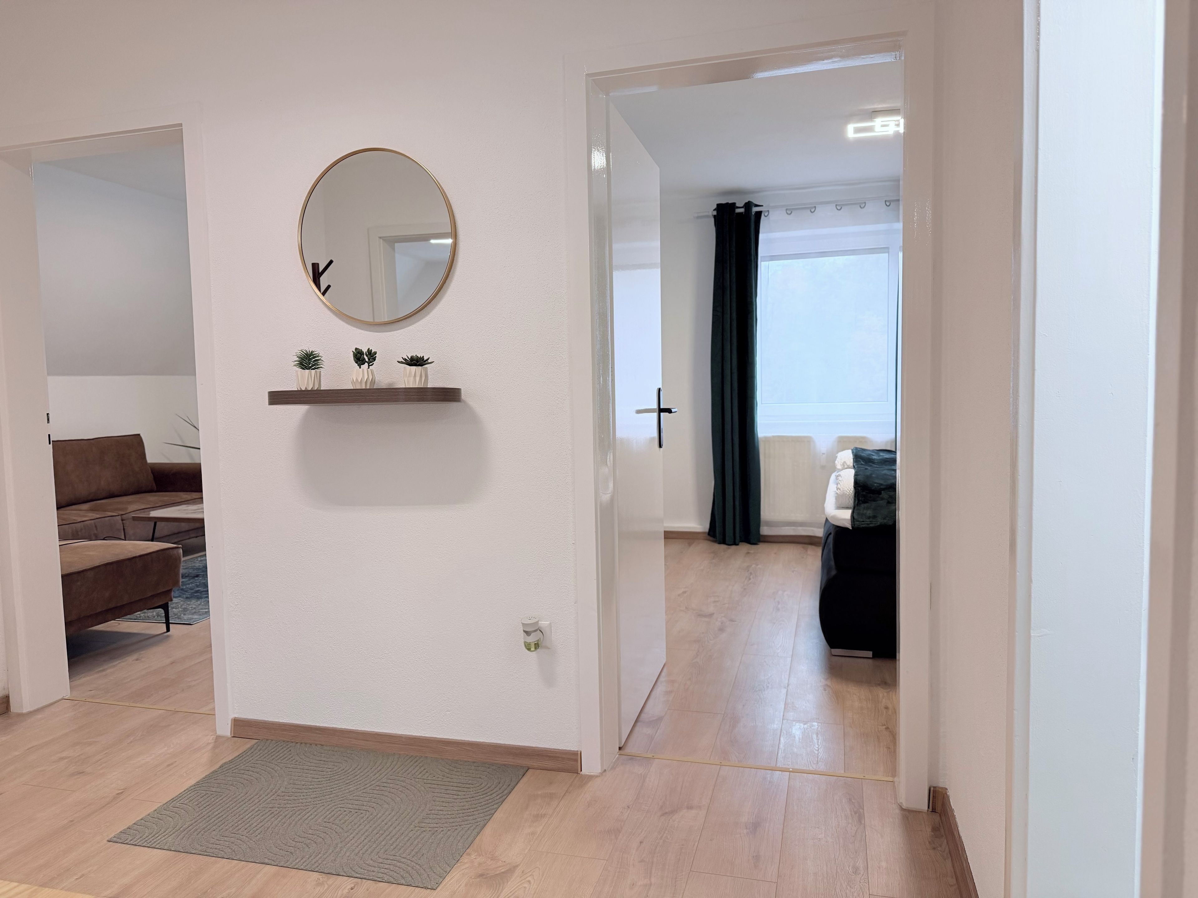 A modern living room with a sofa, a coffee table, a mirror, and a shelf with small plants.