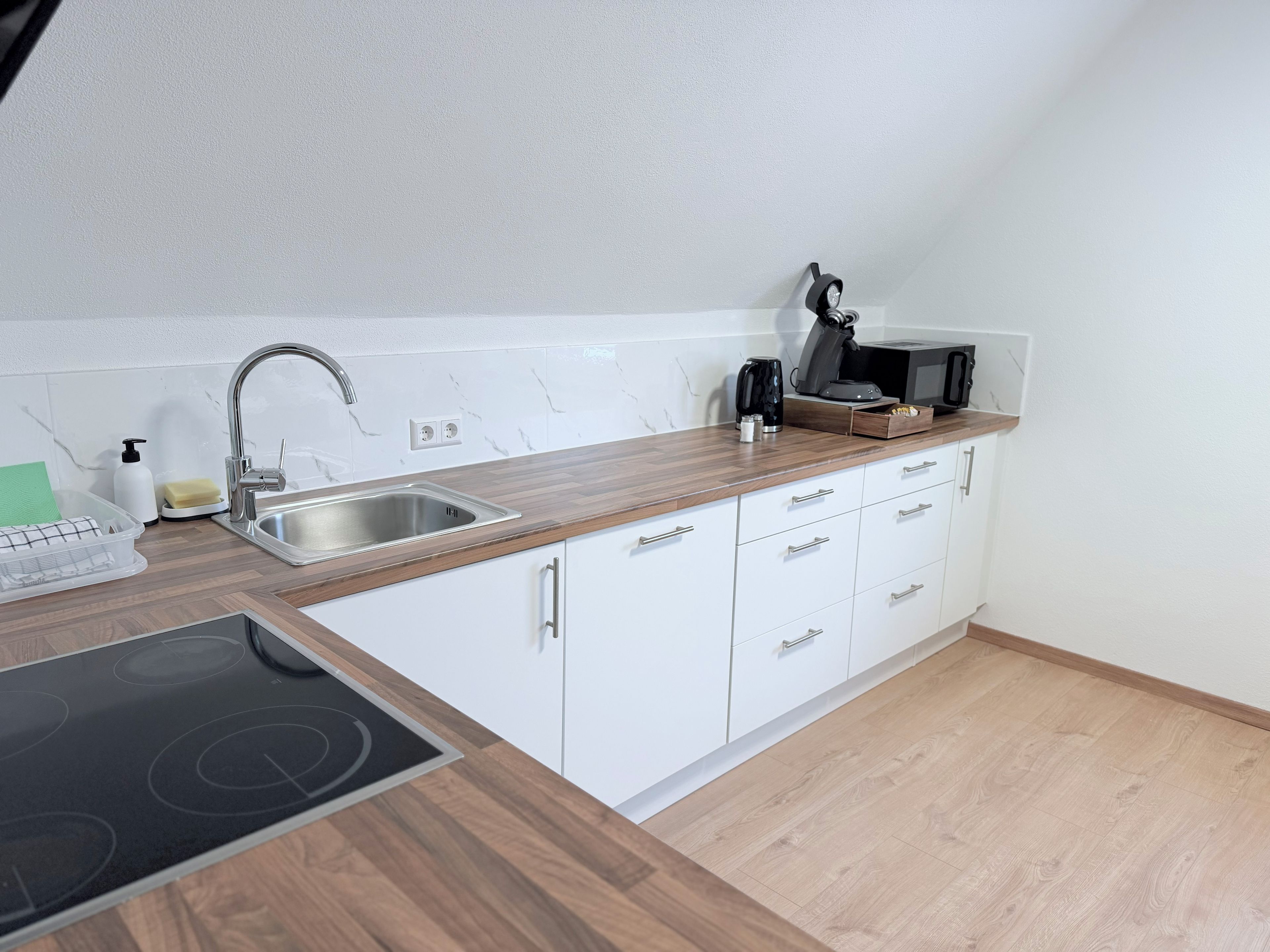 Een moderne keuken met een roestvrijstalen spoelbak, een houten aanrechtblad, witte kasten en een geïntegreerd inductiekookveld.