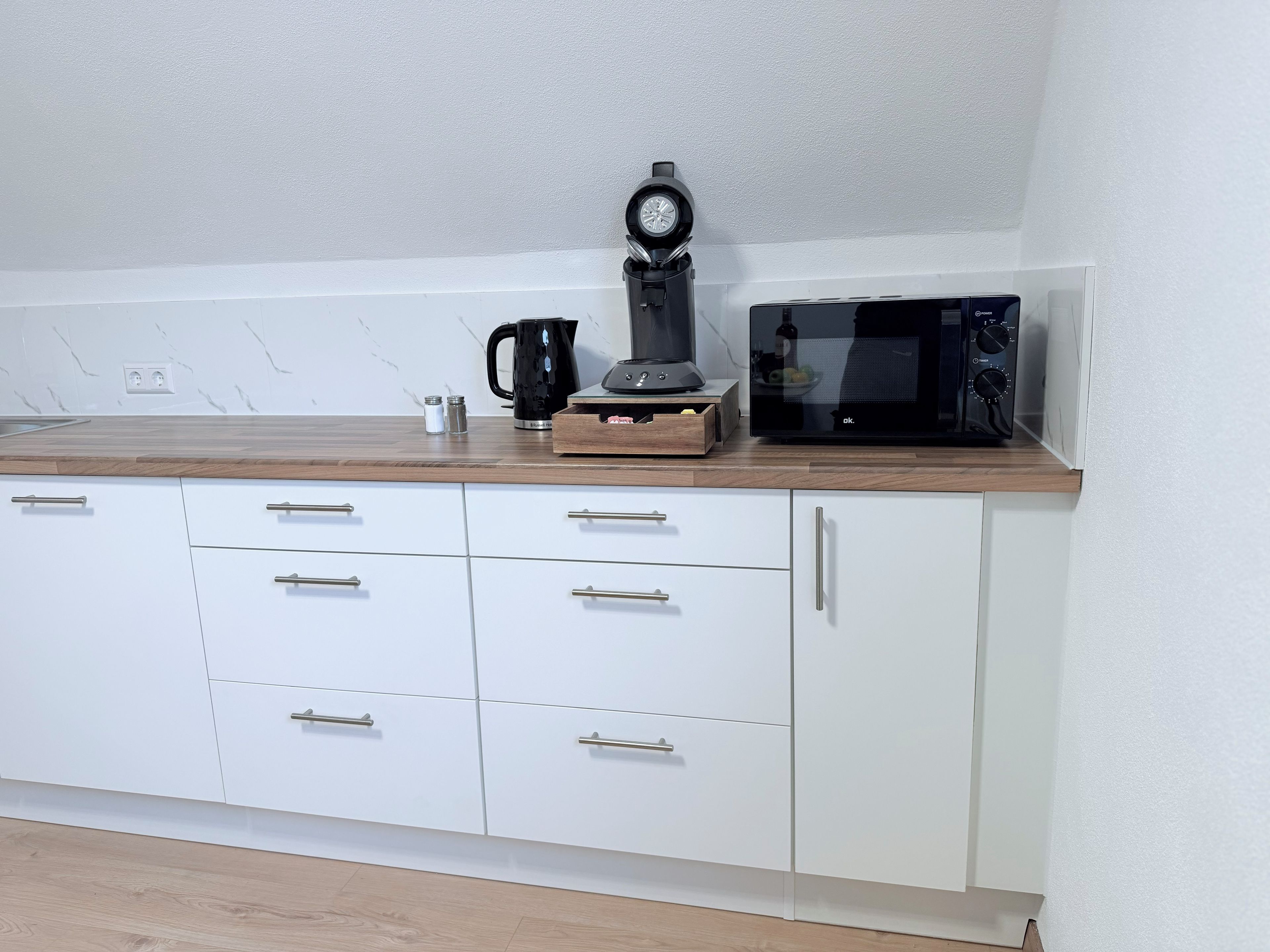 A kitchen with white cabinets, a microwave, a coffee maker, and a wooden countertop.