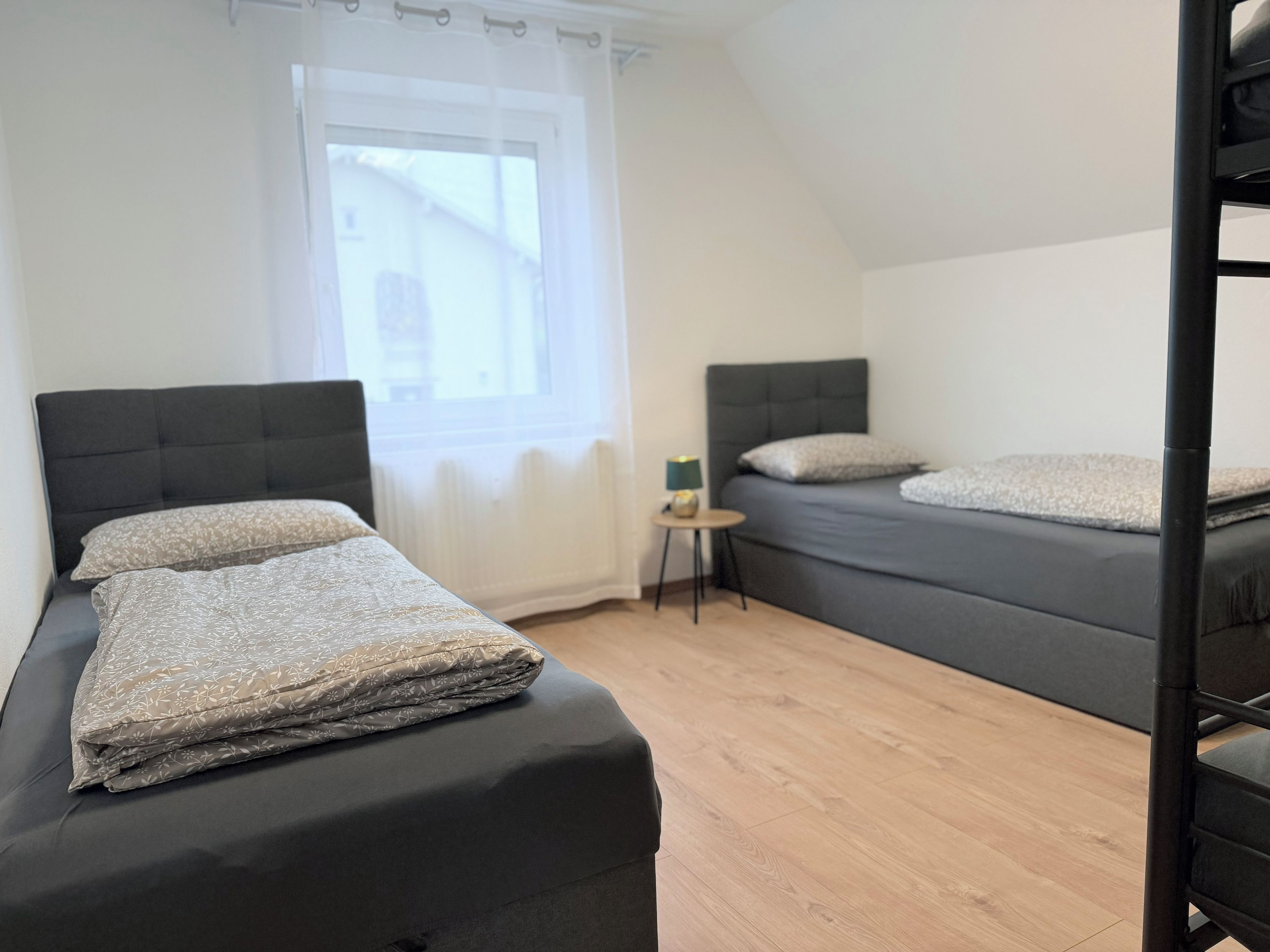 Ein Zimmer mit zwei Betten, einem kleinen Tisch und einem Fenster.