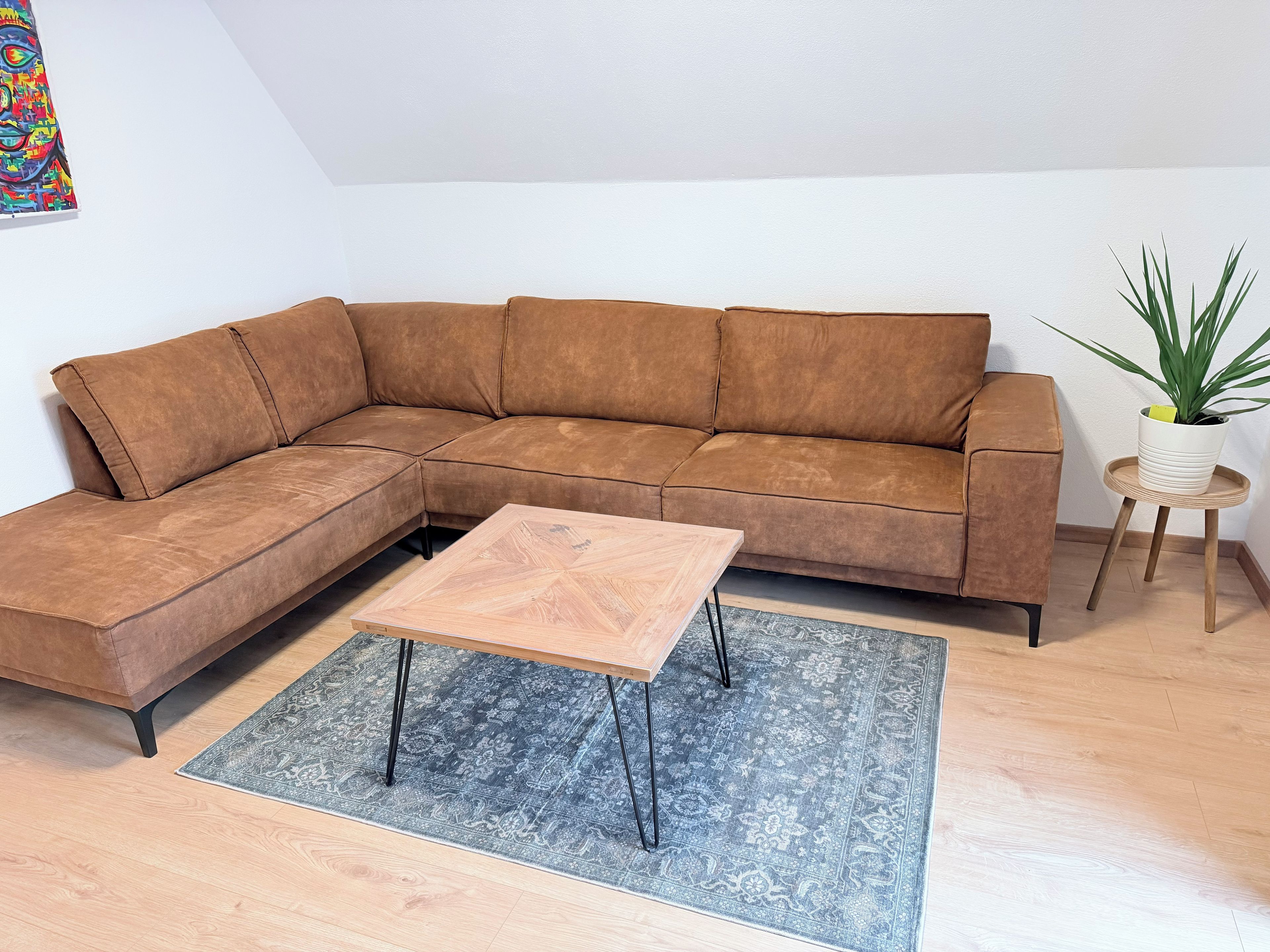 A sectional sofa with a matching ottoman, a small wooden coffee table, a patterned rug, and a potted plant on a wooden floor.