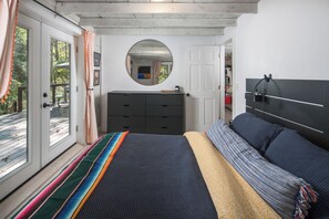 Ein Schlafzimmer mit einem großen Bett, einem Schminktisch, einem Spiegel und Blick ins Freie.