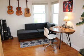 Un salon avec un canapé foncé, une table ronde sur laquelle se trouve une lampe, et trois guitares accrochées au mur.