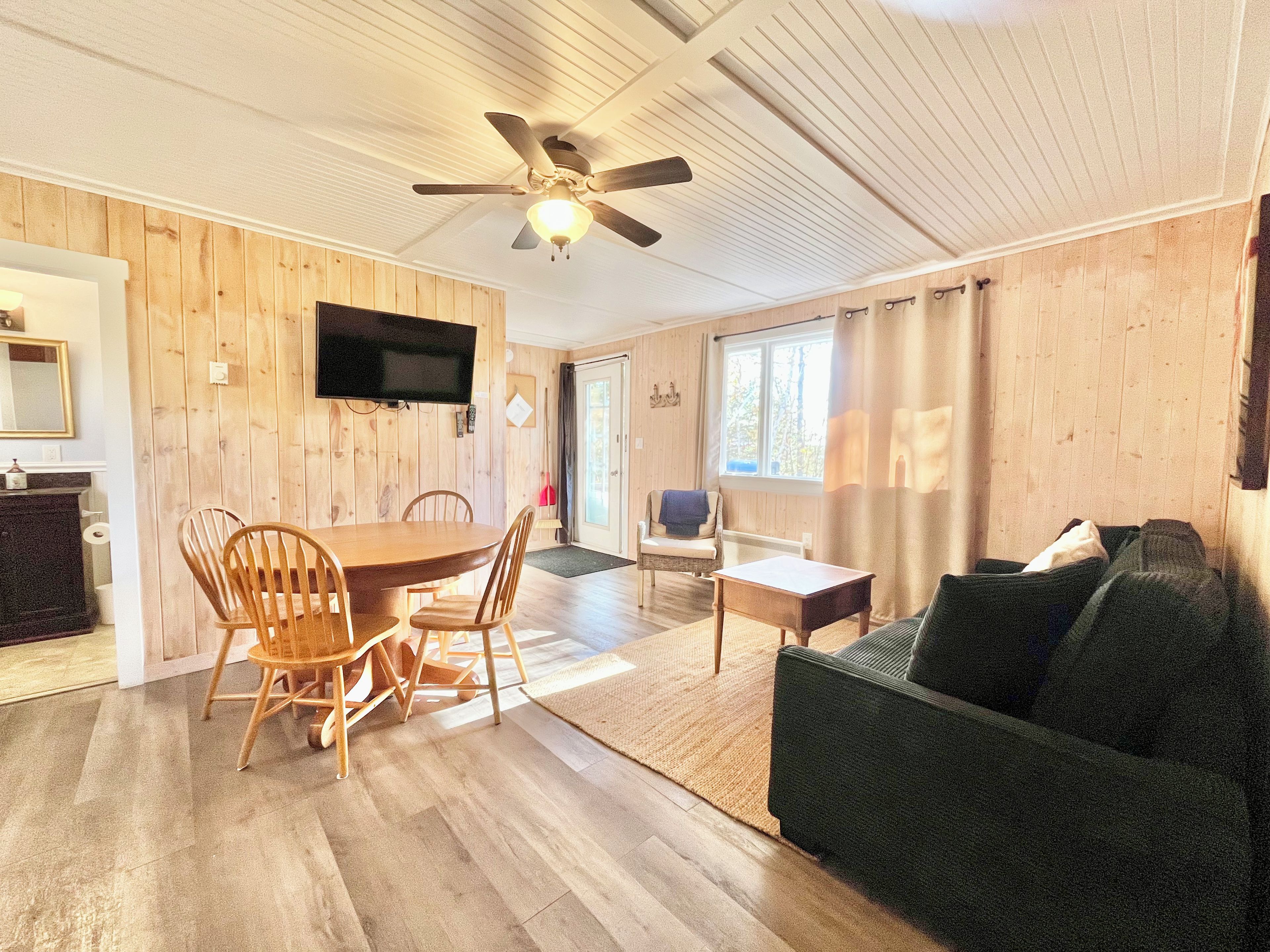 A room with a dining table, chairs, a sofa, a television, and a ceiling fan.