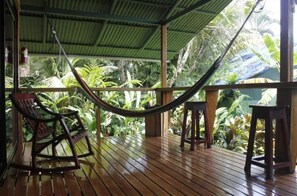 A wooden deck with a hammock, chairs, and a view of lush tropical vegetation.