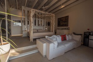 A modern bedroom with a canopy bed, a sofa, and a small kitchenette.