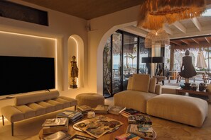 A modern living room with a flat-screen TV, comfortable seating, a statue, and a view of the outdoors.