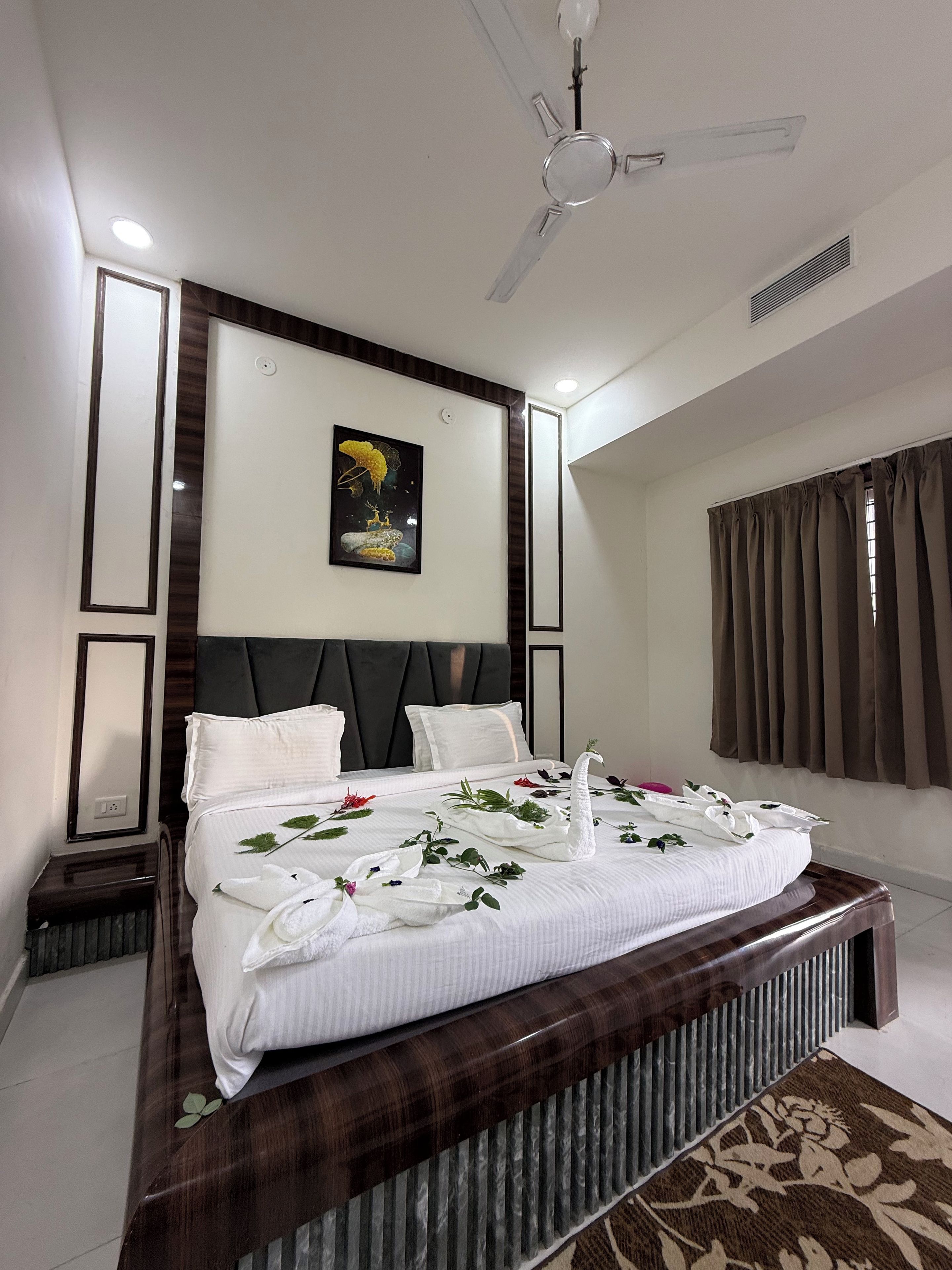 A modern hotel room with a large bed, a ceiling fan, a painting on the wall, and a window with curtains.