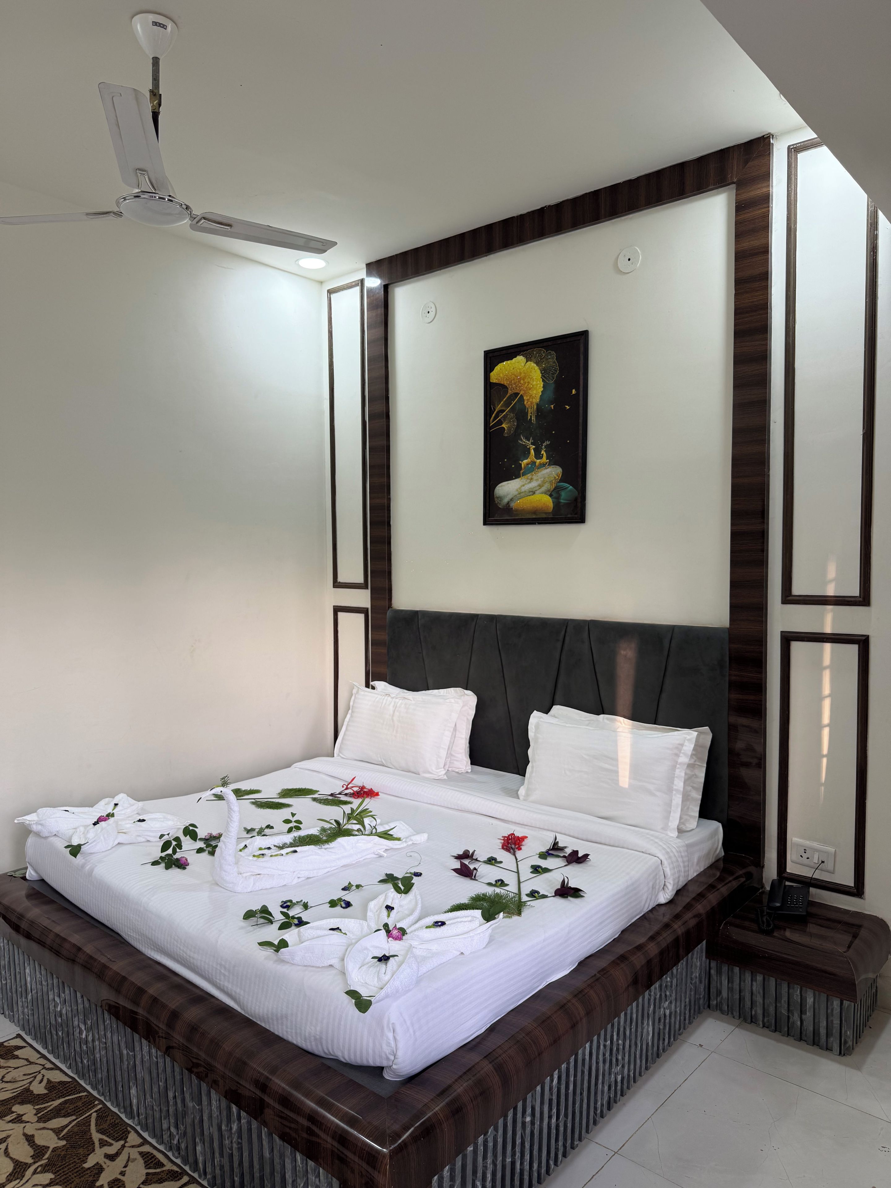 A neatly made bed with white linens and decorative towels, a dark headboard, and a painting on the wall.
