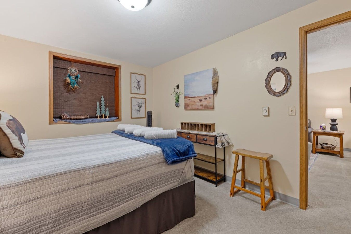 A bedroom with a bed, a nightstand, a dresser, a window with a view, and a door leading to another room.