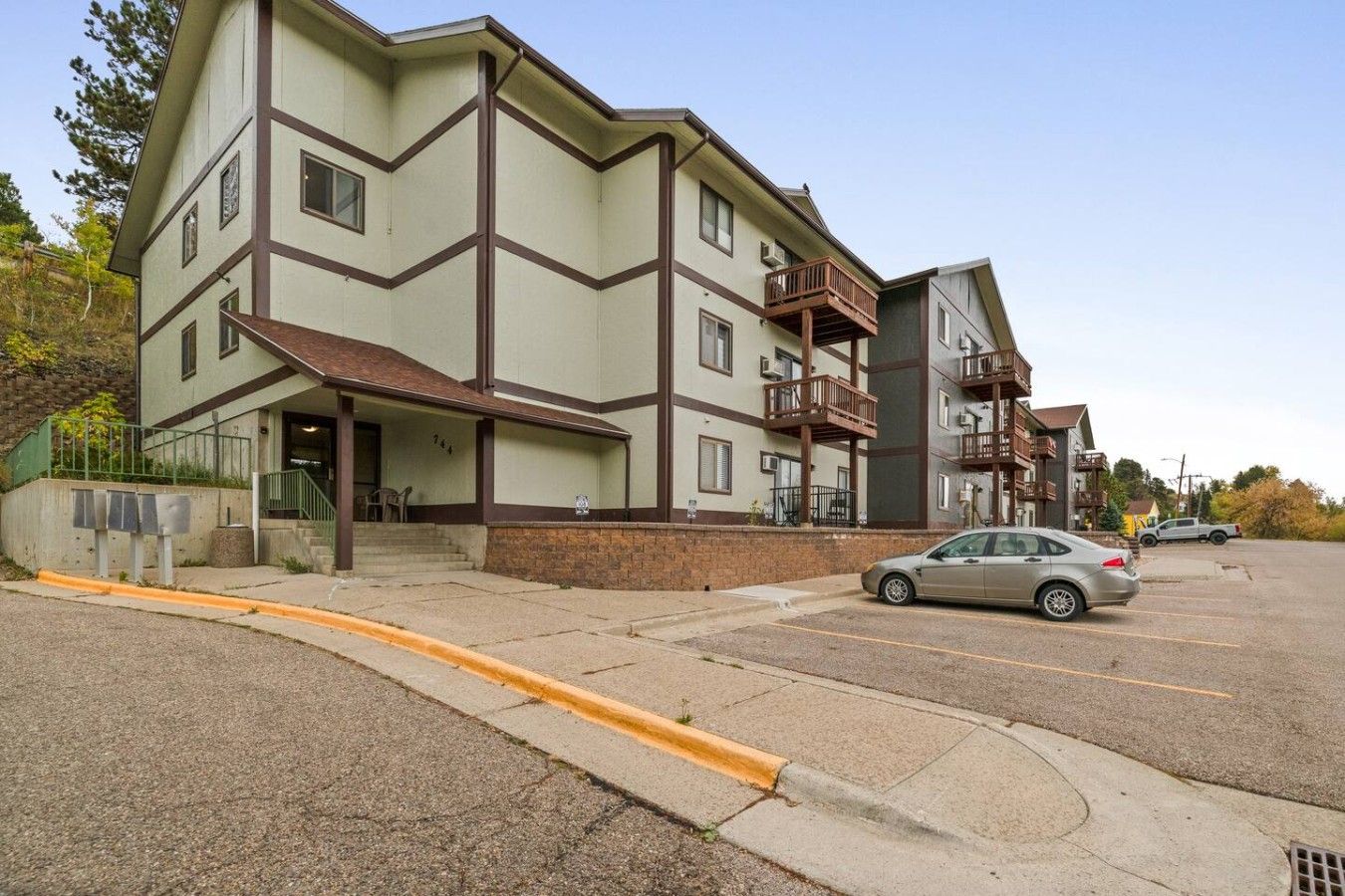 A multi-story building with a flat roof, a covered entrance, and a parking lot with a car.