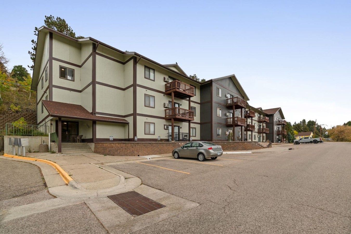 A multi-story residential building with a flat roof, balconies, and a parking area.