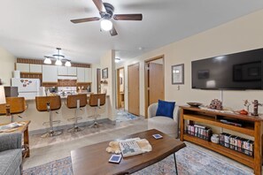A modern living room with a flat-screen TV, a coffee table with books, and a bookshelf. - Condo: 1 bed, 1 bath, DVD Library, Fishing Gear (Lead)