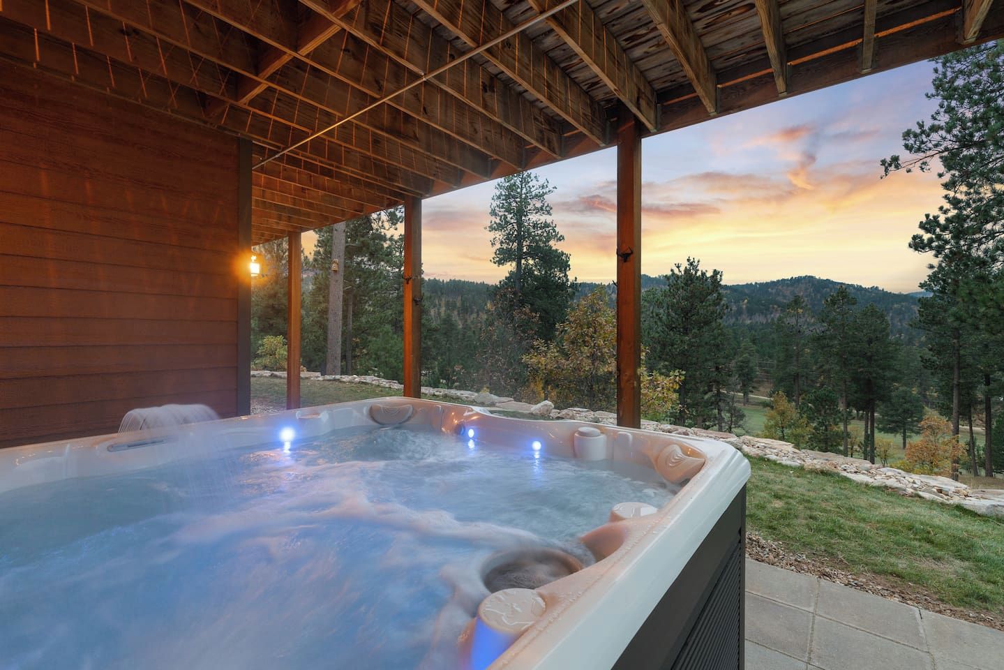 A hot tub with a sunset view, wooden beams, and a stone wall.