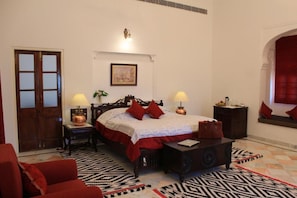Ein Schlafzimmer mit einem Bett, zwei Nachttischen, einem kleinen Tisch, einem roten Sofa und einem gemusterten Teppich.