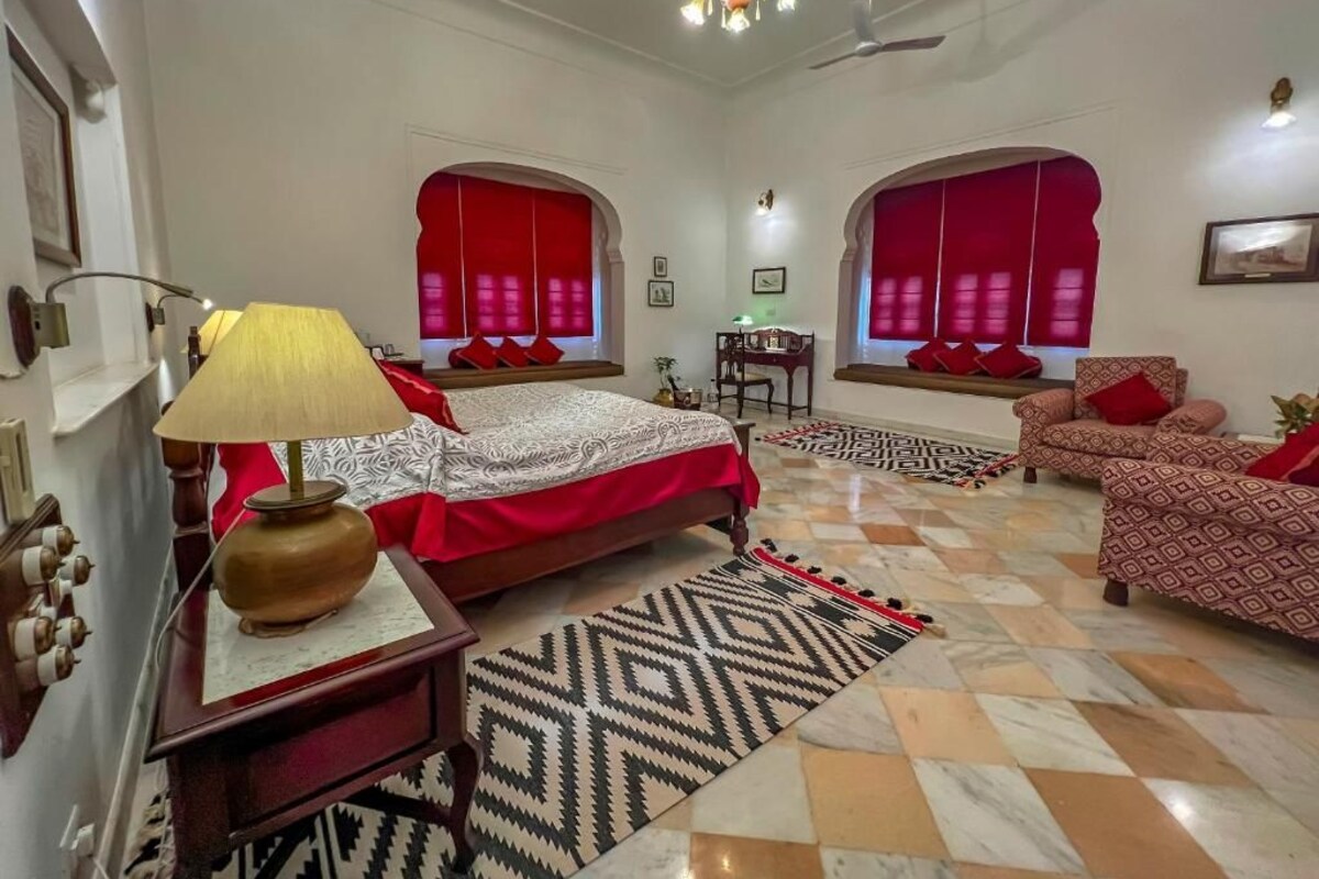 Une chambre spacieuse avec un grand lit, deux canapés, un bureau et un lustre.