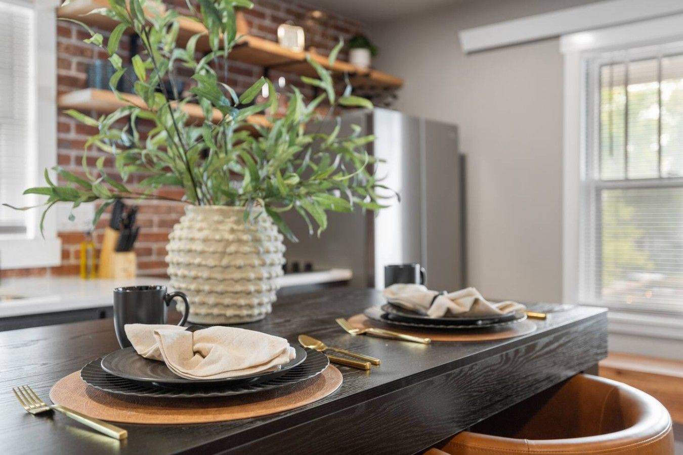 Una cocina moderna con encimera oscura, una planta en maceta y una vajilla con platos y cubiertos.