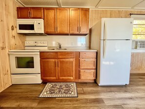 Une cuisine avec des meubles en bois, un four à micro-ondes, un four traditionnel, un réfrigérateur et un tapis à motifs.