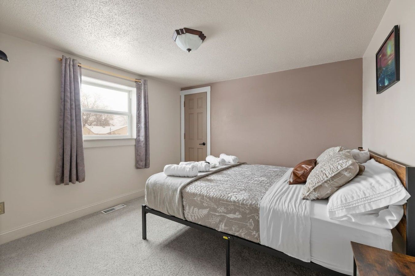 A bedroom with a bed, a window with curtains, a door, and a ceiling light fixture.