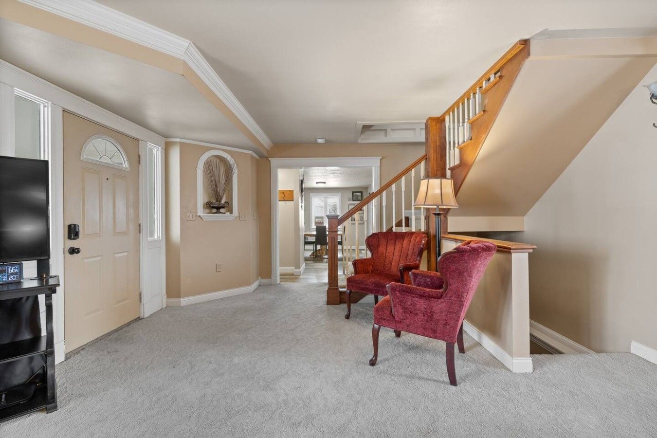 A spacious hallway with a carpeted floor, a staircase with wooden railings, and two red upholstered chairs.