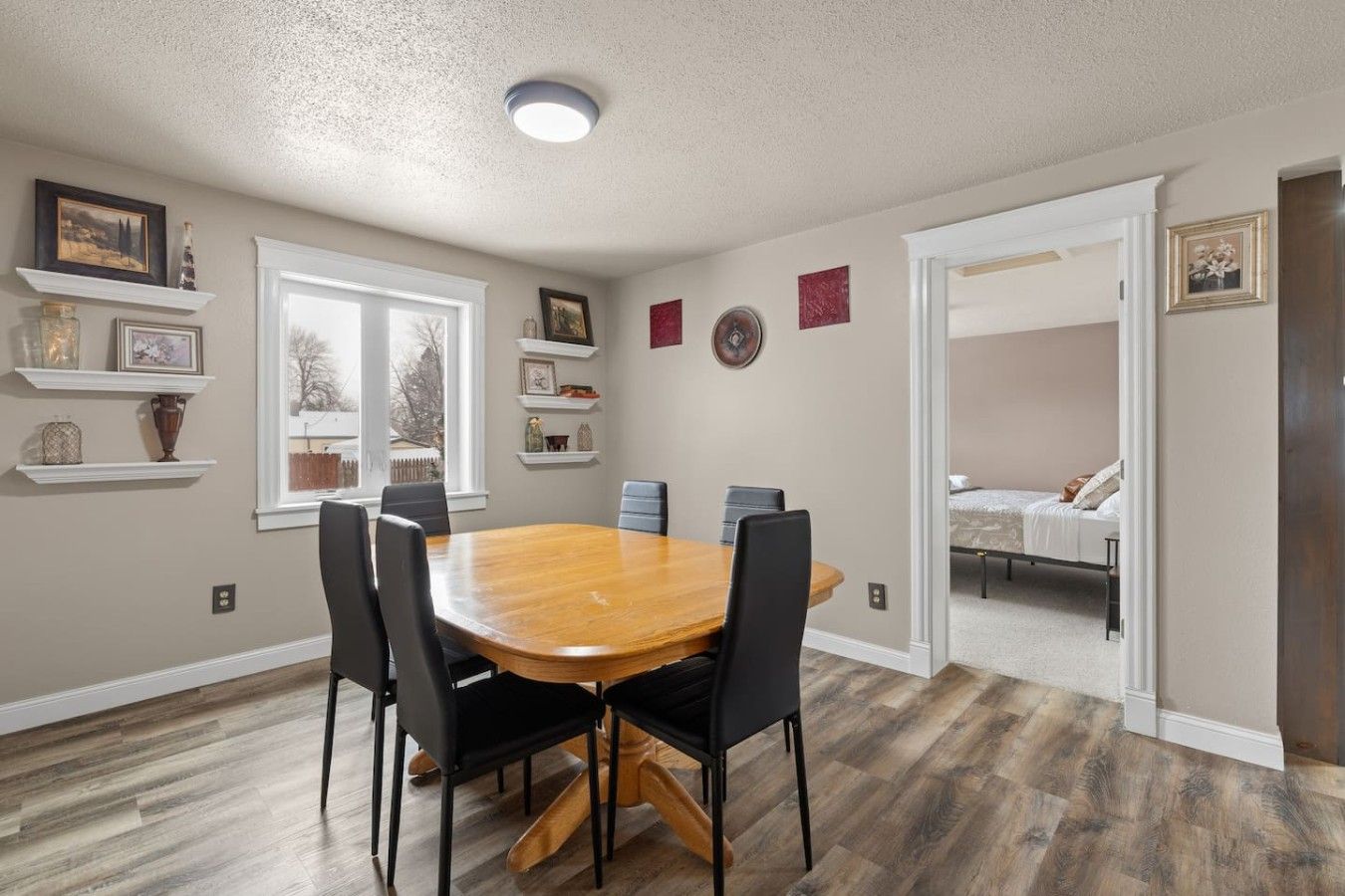 A dining area with a wooden table and chairs, a window with a view, and a door leading to a bedroom.