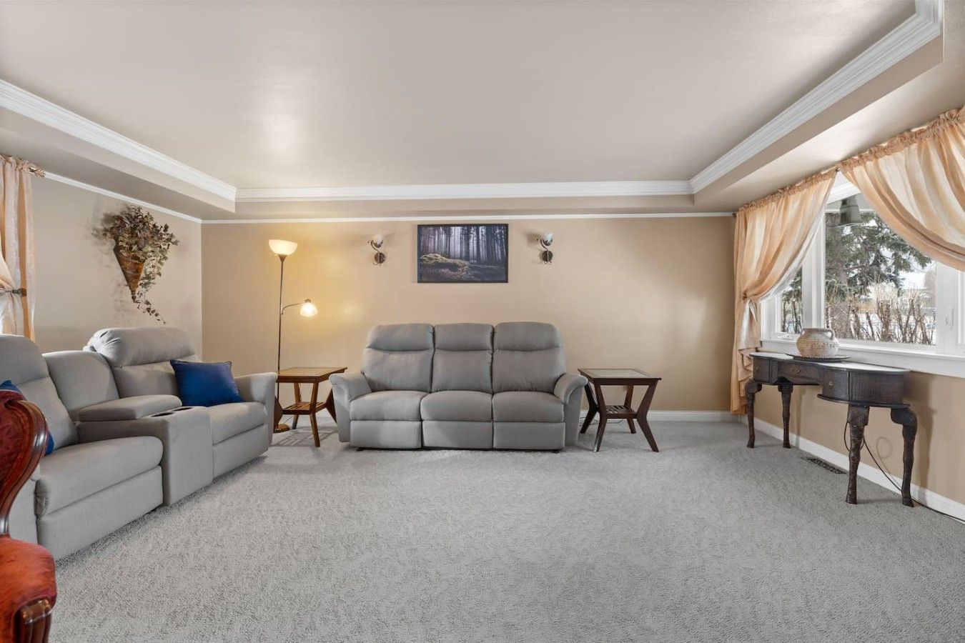 A living room with a grey sofa, a smaller armchair, a coffee table, and a side table. There is a painting on the wall and a floor lamp.