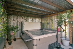 Ein Whirlpool mit Holzboden und -wänden, verziert mit vertikalen Jalousien und hängenden Pflanzen.