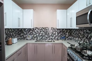 Una cocina moderna con armarios blancos, un salpicadero de mosaico blanco y negro, un lavamanos de acero inoxidable y una estufa a gas.