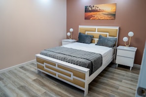 Un dormitorio con cama, mesitas de noche, un cuadro y suelo de madera.