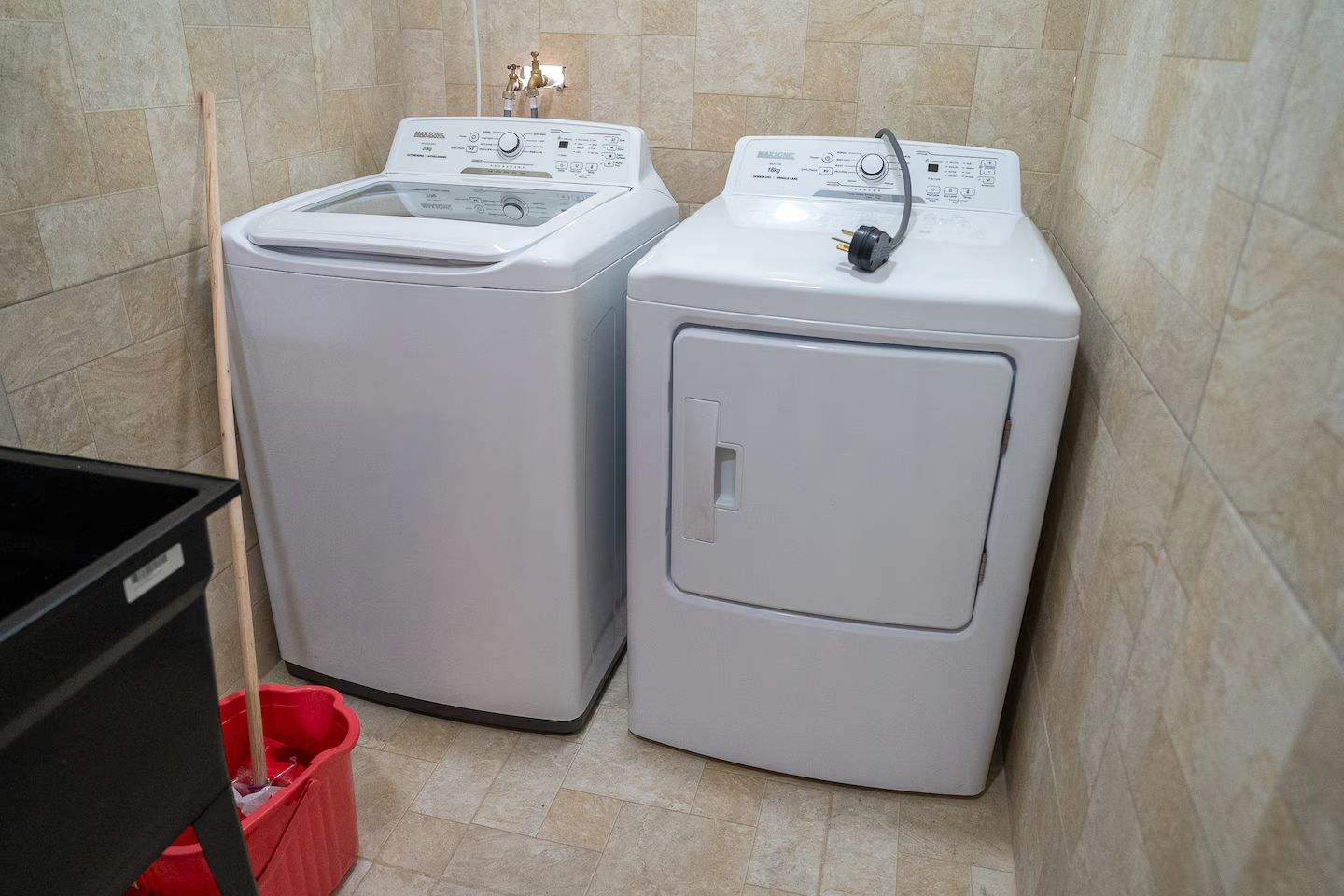 Two front-loading washing machines in a corner of a room with tiled walls and a red trash bin.